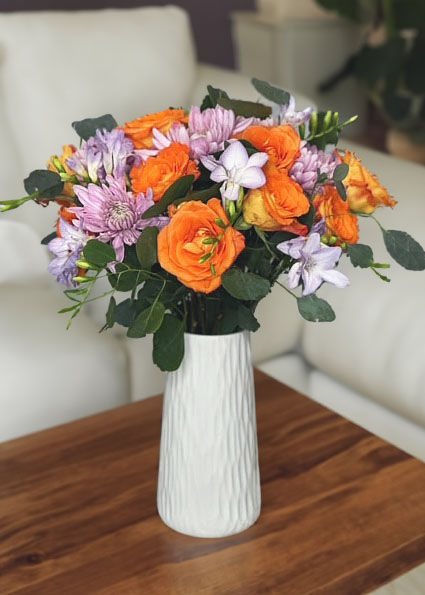 Orange Roses, Pink Mums, Purple Freesia, Eucalyptus, white Vase, Summer and Spring Bouquet, Bright and Cheerful Flower arrangement, Home decor, Beautiful flower arrangement on wooden table with white couch in background