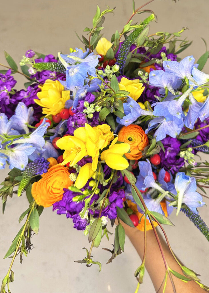 orange ranunculus, yellow freesia, delphinium, eucalyptus, hypericum berries, stock flower 