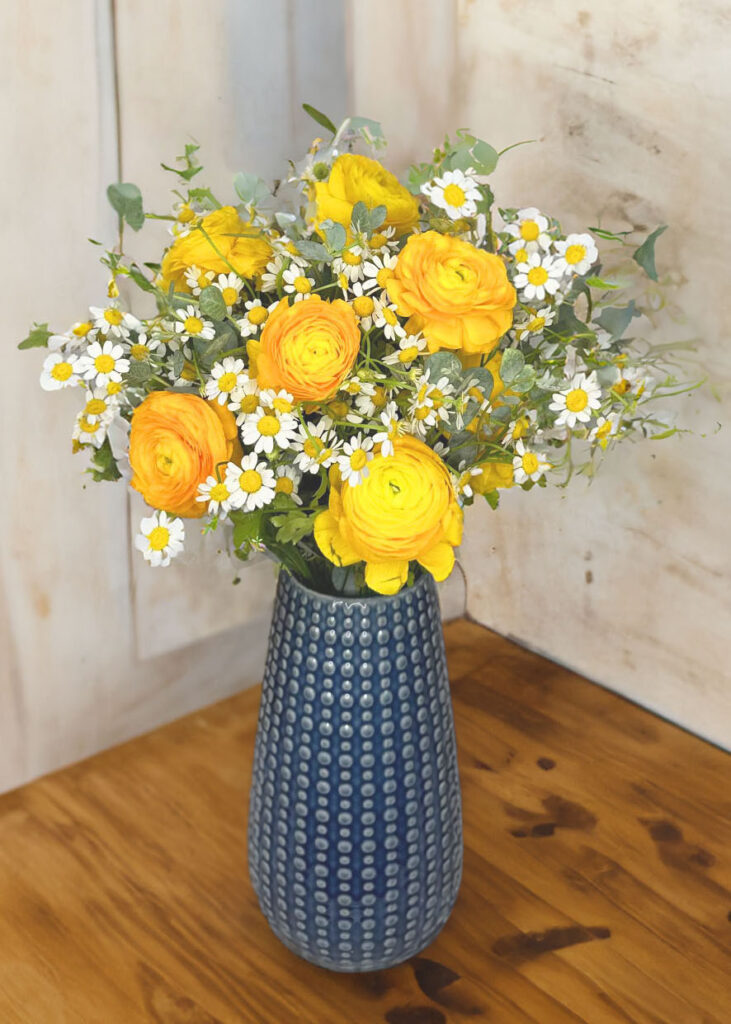 yellow ranunculus, daises, eucalyptus in a blue textured vase. 